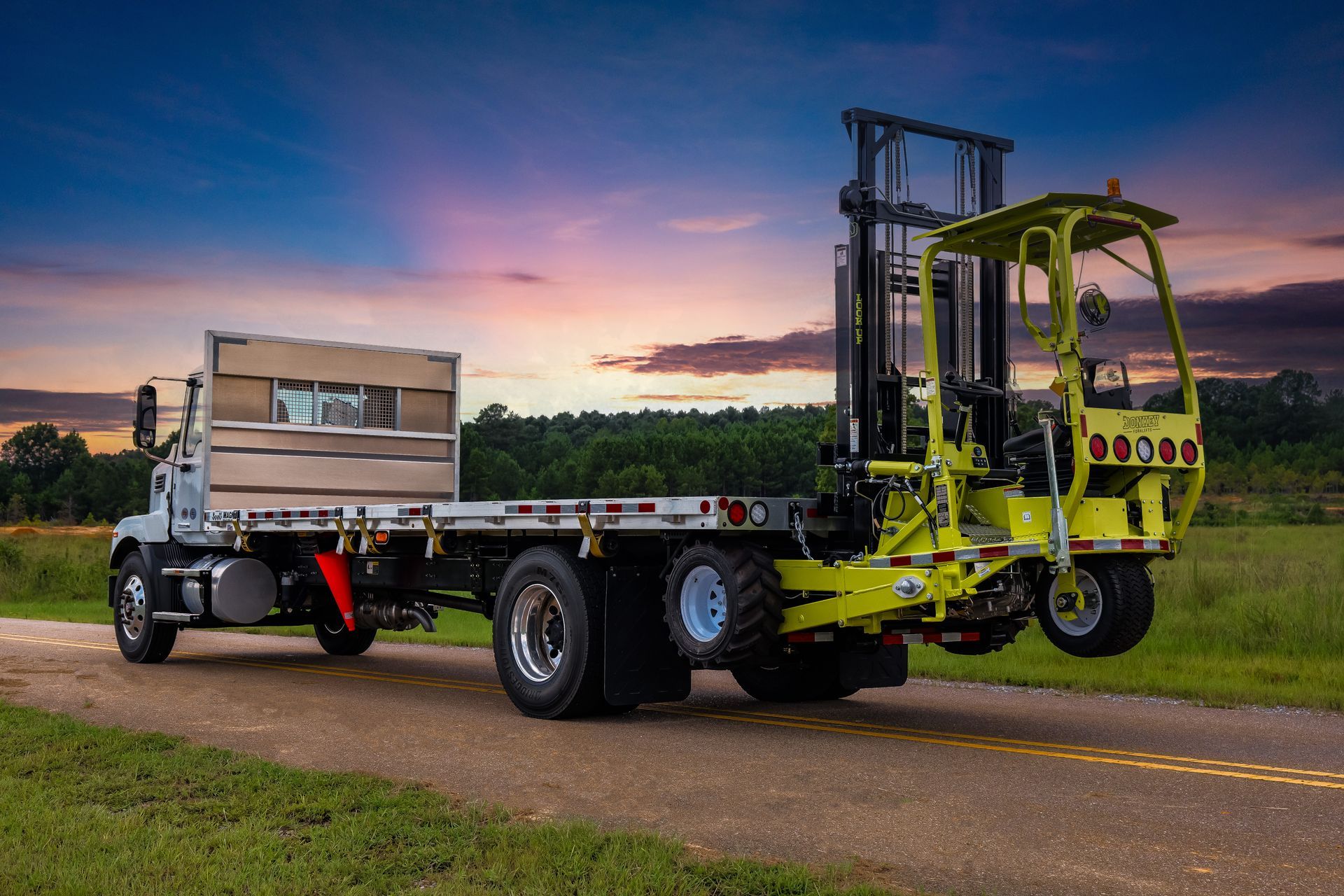 Truck with a mounted forklift on a rural road at sunset. The forklift is neon green.