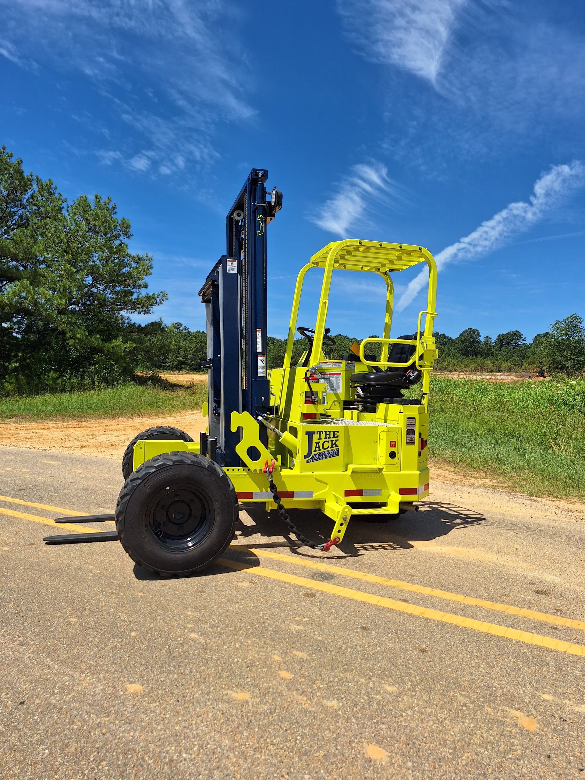 Bright yellow forklift with black tires on a paved road under a blue sky.