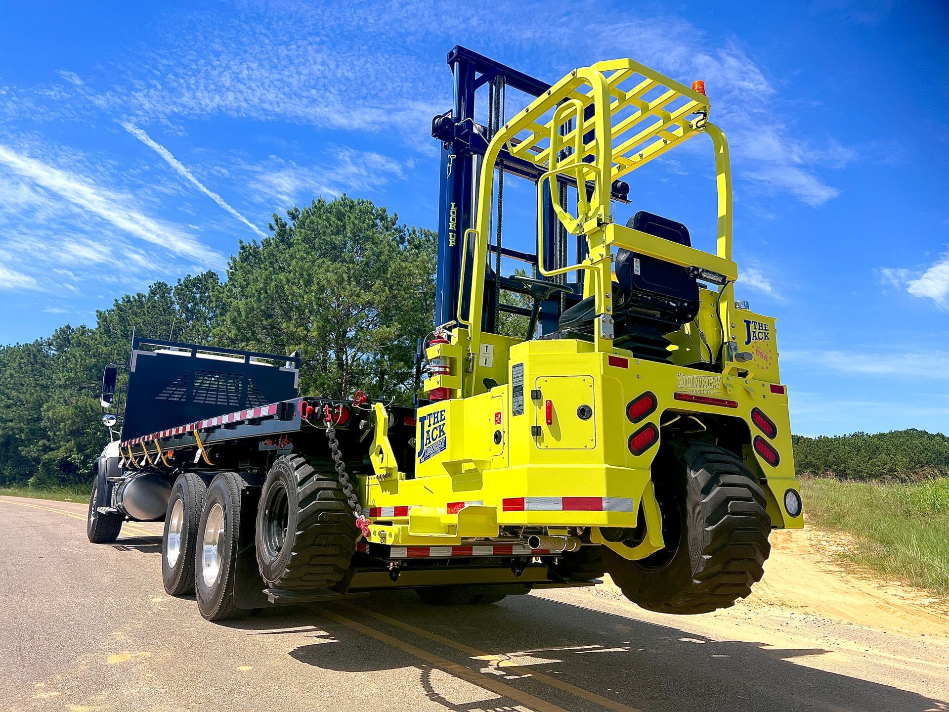 Yellow forklift on a flatbed trailer, under a bright blue sky.