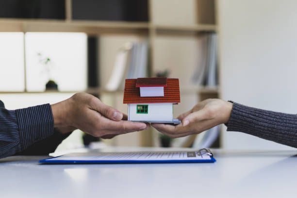 A Man Is Handing A Model House To A Woman — Dallas, TX — Misteli Law Firm