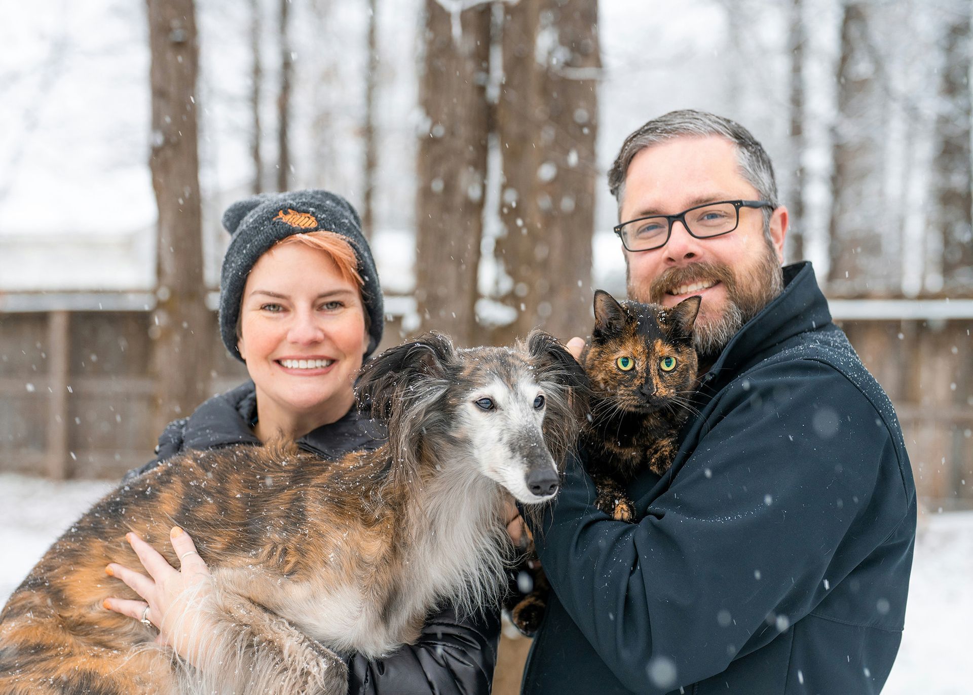 image of a couple in the snow with their dog and cat
