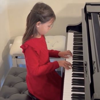Young girl in red dress playing a piano, indoors.