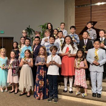 Children in formal attire with trophies, on a stage.