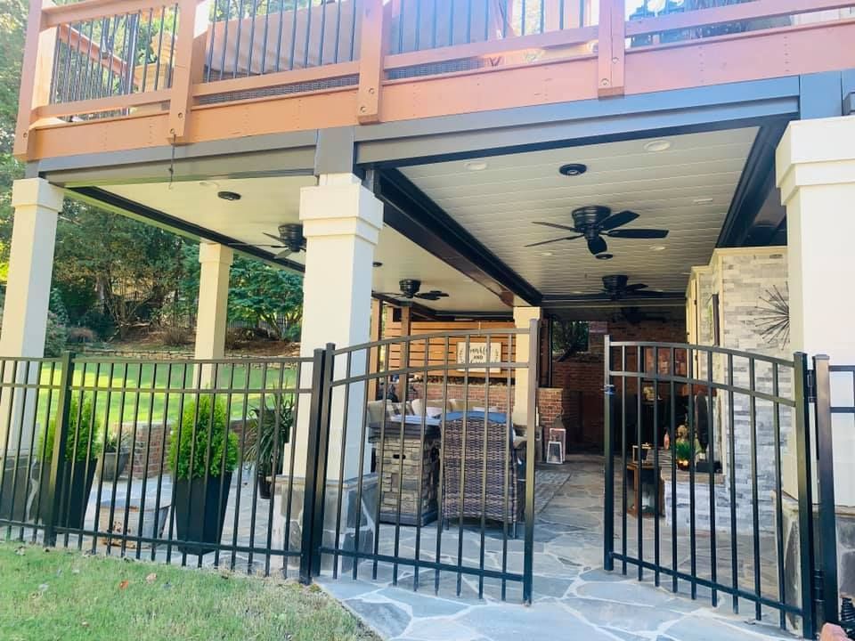 A fence surrounds a patio area with a wooden deck and a ceiling fan.