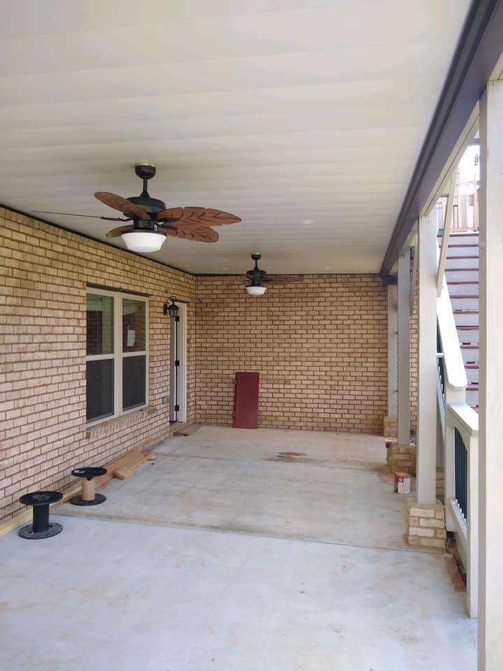 There are two ceiling fans on the porch of a brick house.