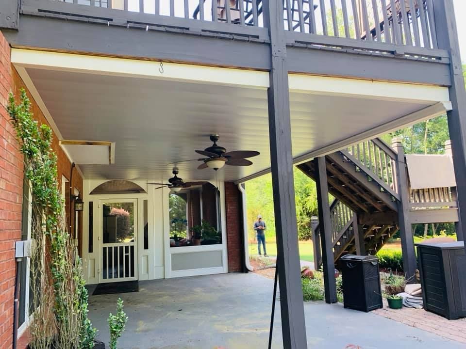 A man is standing under a covered porch with a ceiling fan.