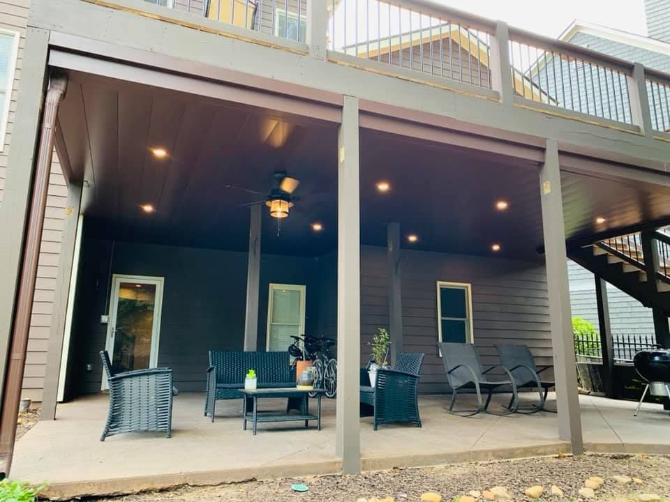 A large covered porch with furniture and a staircase leading to the second floor of a house.