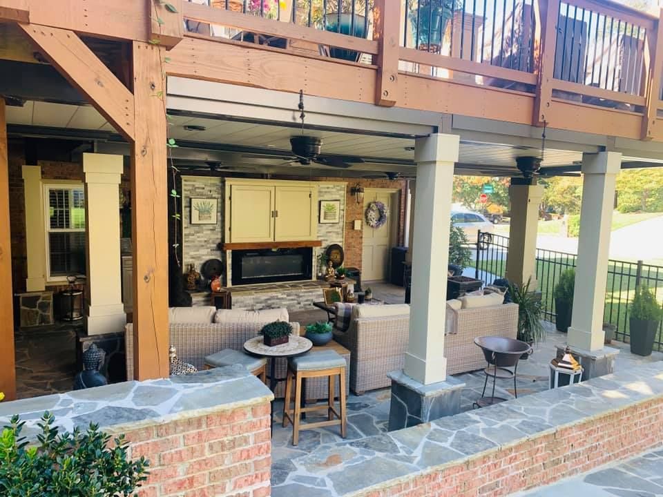 A large covered patio with a fireplace , couch , table and chairs.