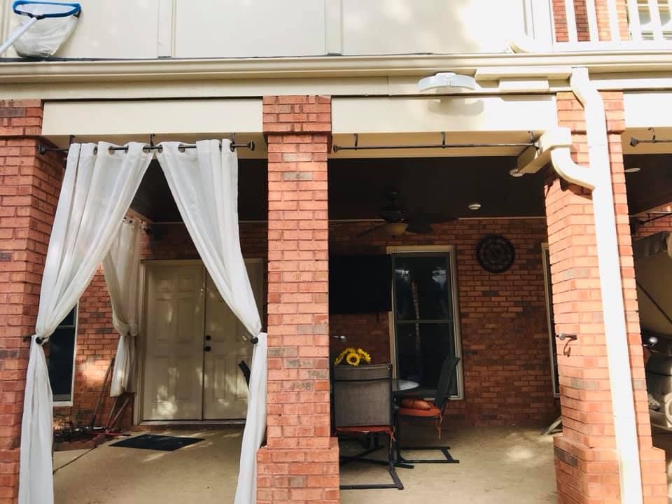 A brick building with white curtains on the porch