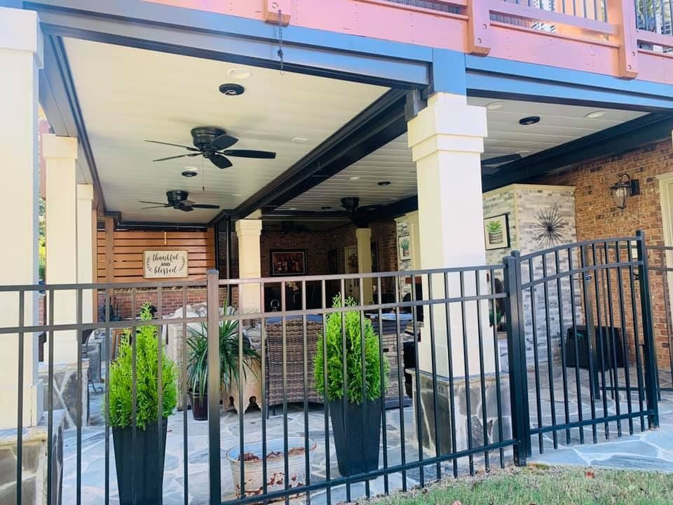 A patio with a ceiling fan and potted plants behind a metal fence.