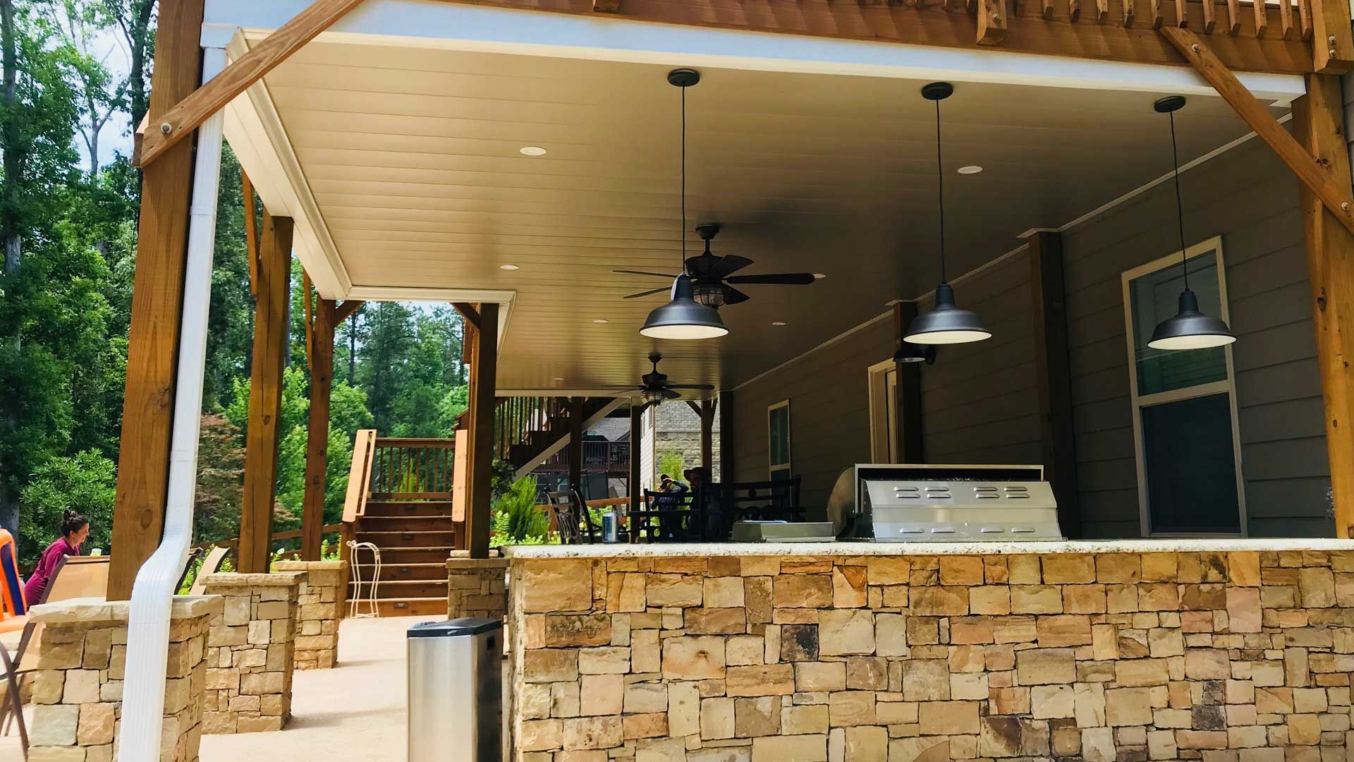 A covered patio with a grill and a ceiling fan.