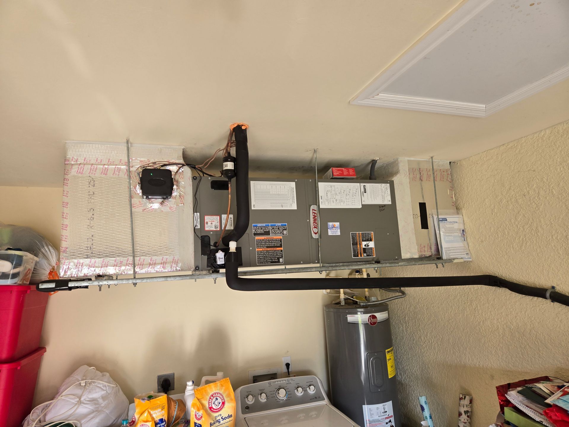 HVAC unit installed in garage ceiling, next to water heater. Ducts and pipes are visible.