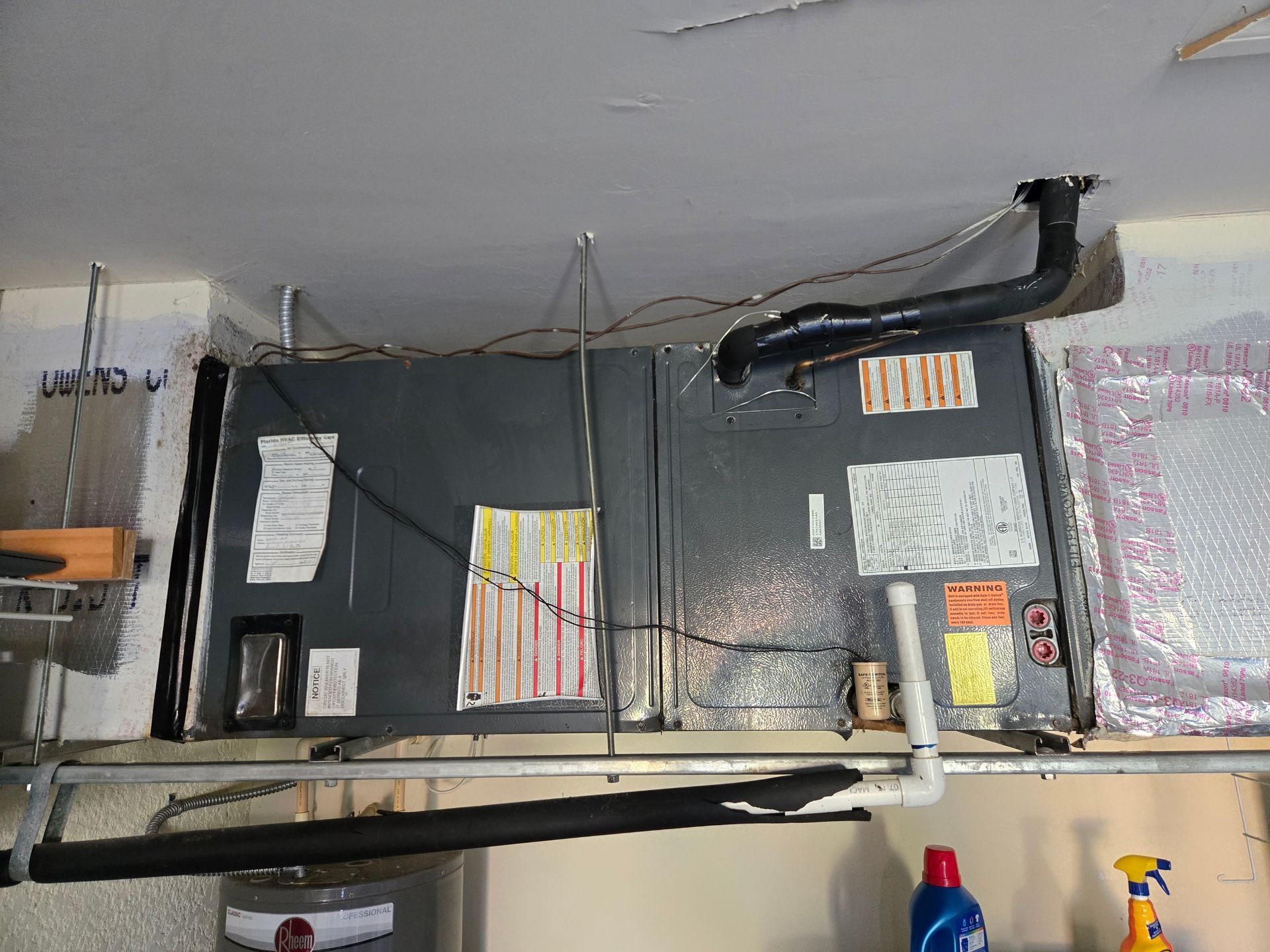 HVAC unit suspended from ceiling in a garage. Ductwork, filter, and water heater are visible.