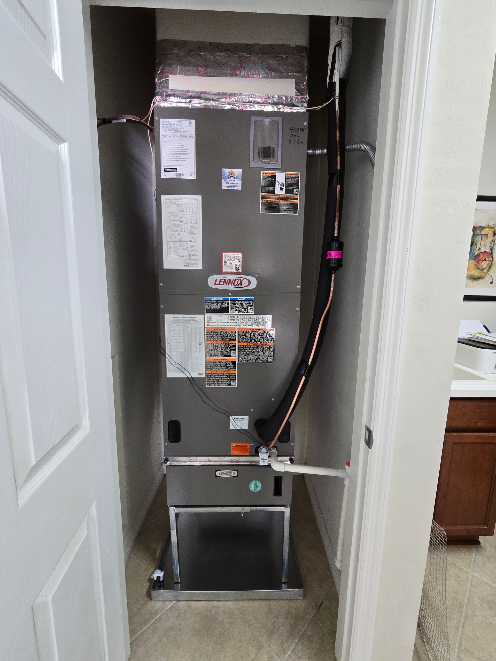 HVAC unit inside a closet. Gray metal box, black insulated ductwork, various labels.