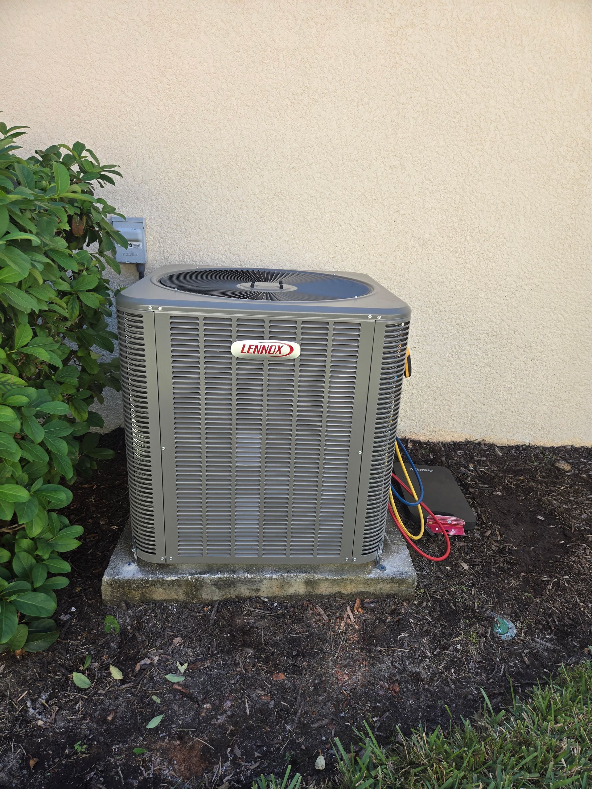 Lennox air conditioning unit outside a building, surrounded by greenery. Grey and beige tones.