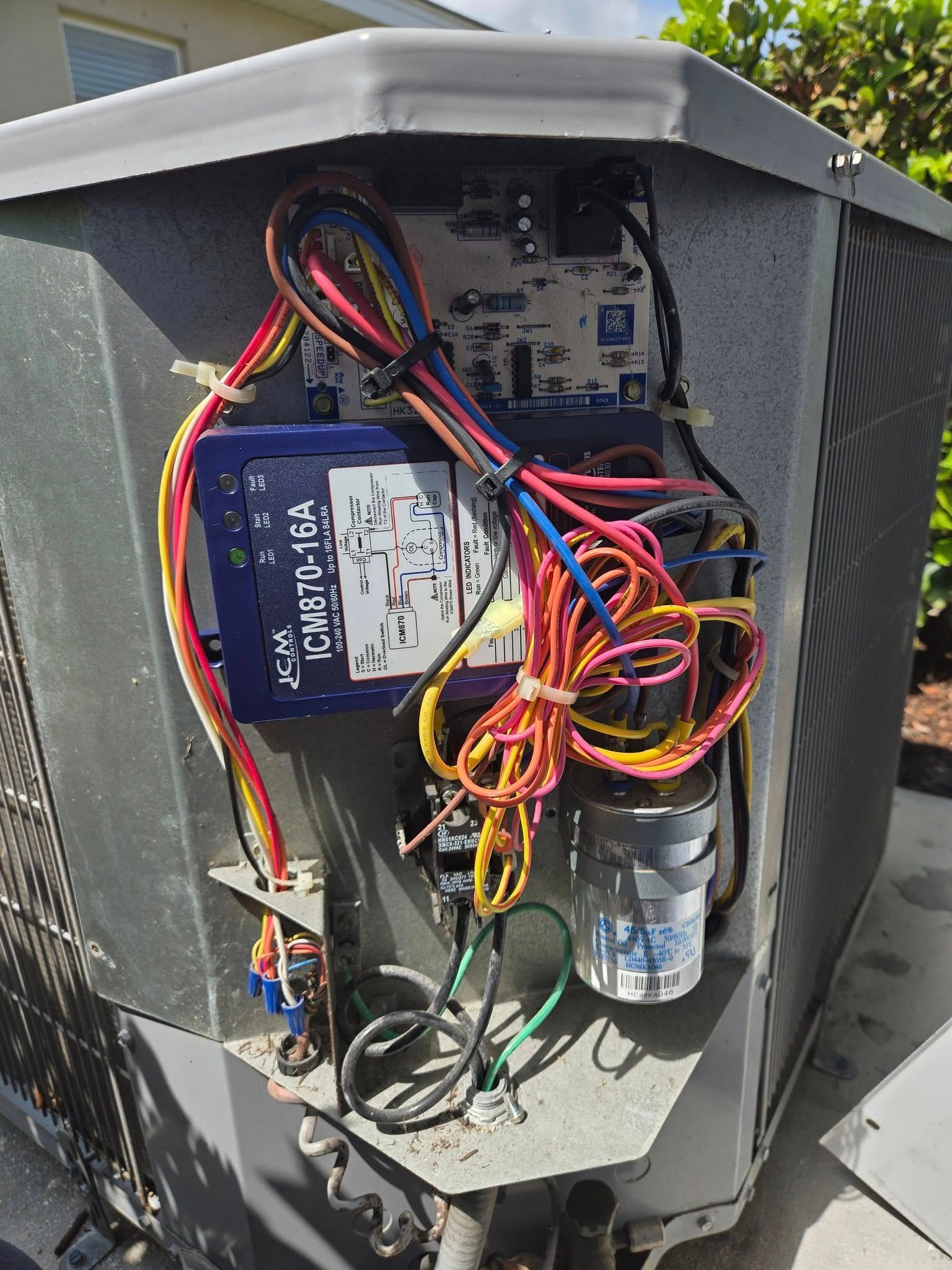 Open air conditioning unit with visible wiring, capacitor, and control box.