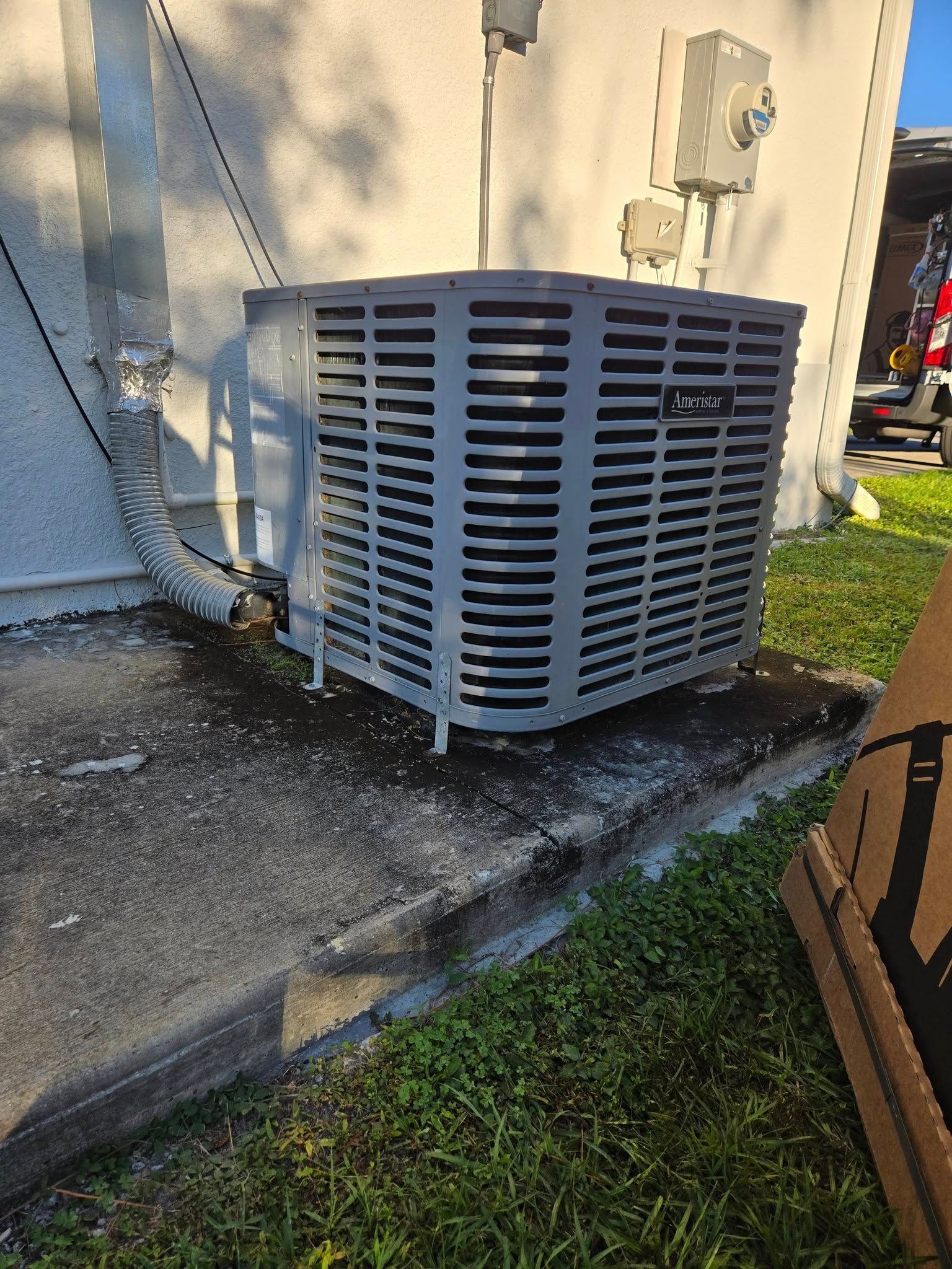 Air conditioning unit outside a building, gray with dark concrete and green grass.