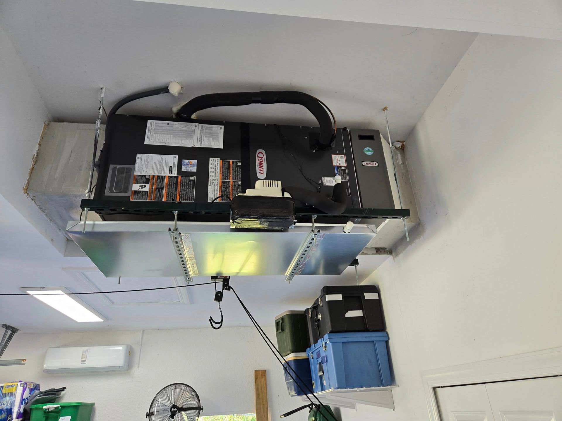 HVAC unit mounted on a garage ceiling, with ductwork and a control panel.