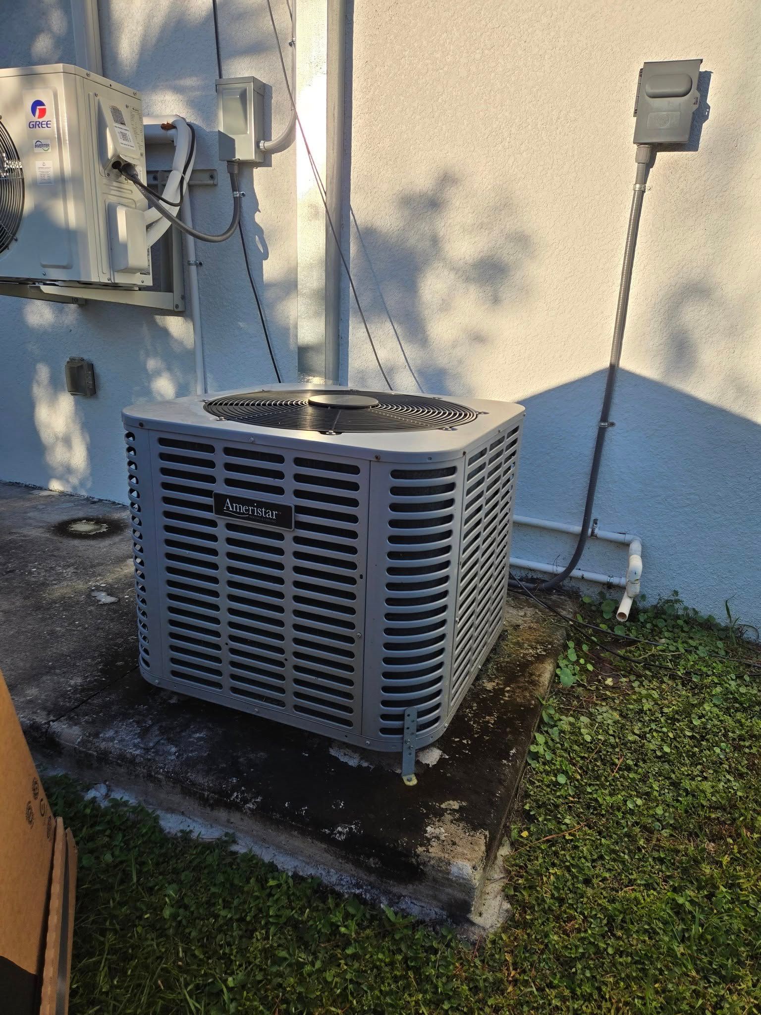 Gray air conditioning unit outside a white building, with a smaller unit above it.