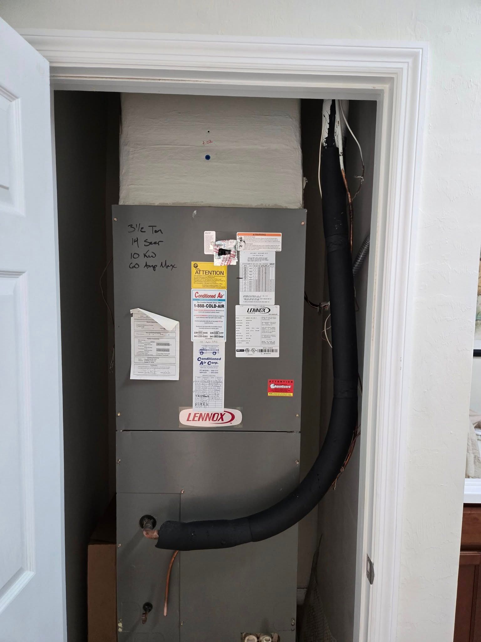 HVAC unit inside a closet. Gray metal box, black insulated ductwork, various labels.
