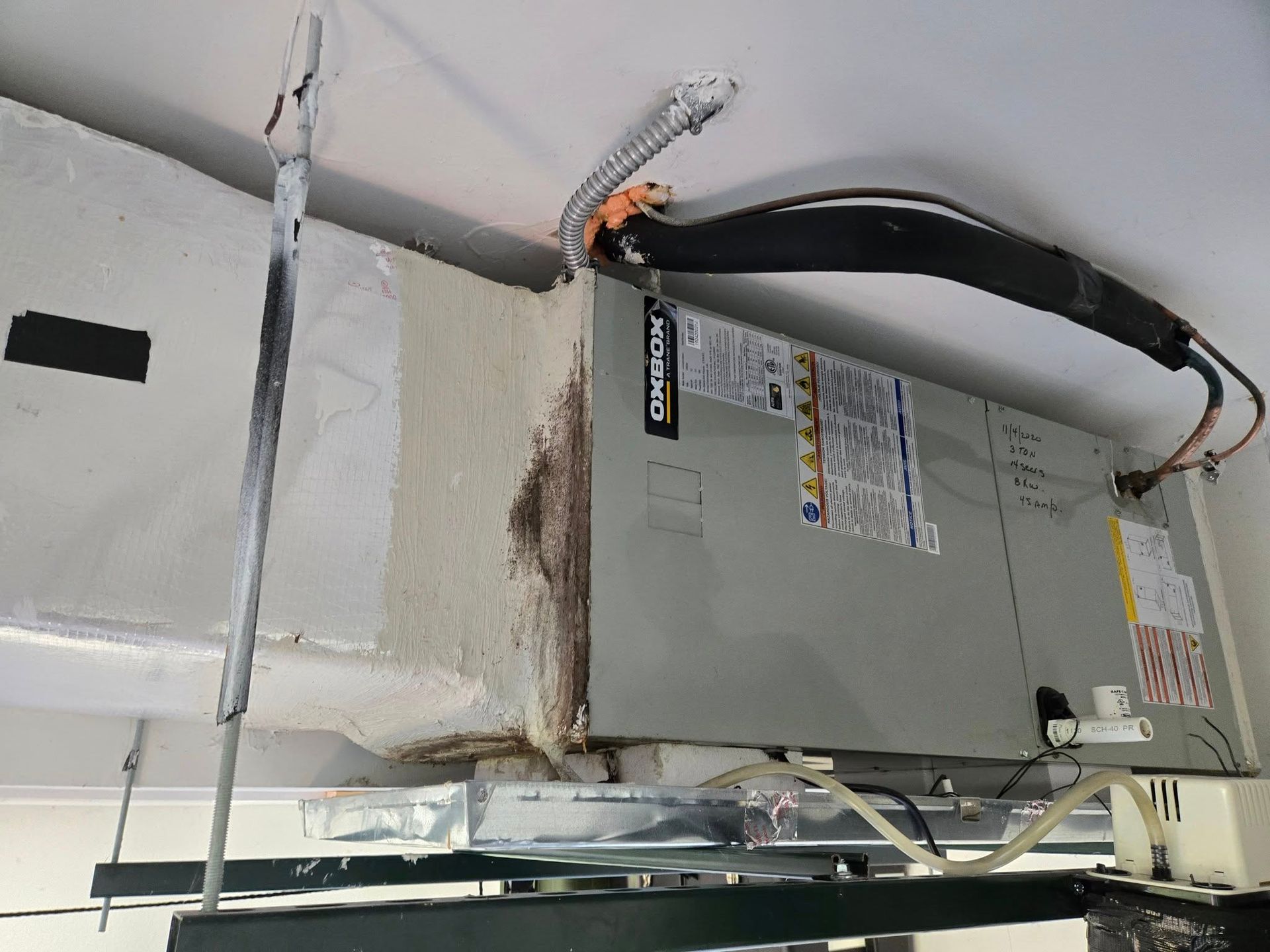 Air conditioning unit mounted on a ceiling, with ductwork and insulated tubing.