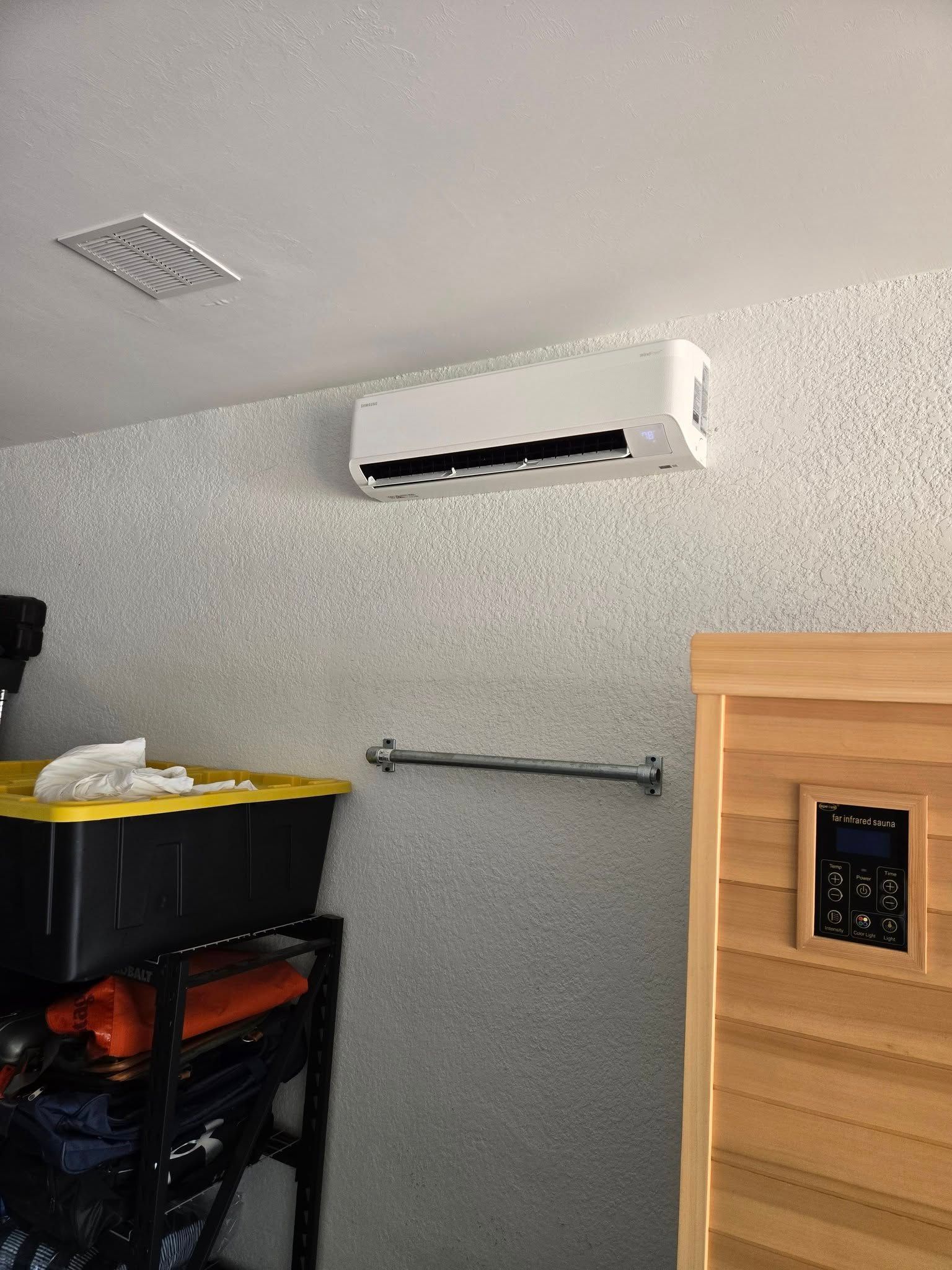 Air conditioning unit mounted on a speckled wall in a room with a sauna and storage shelving.