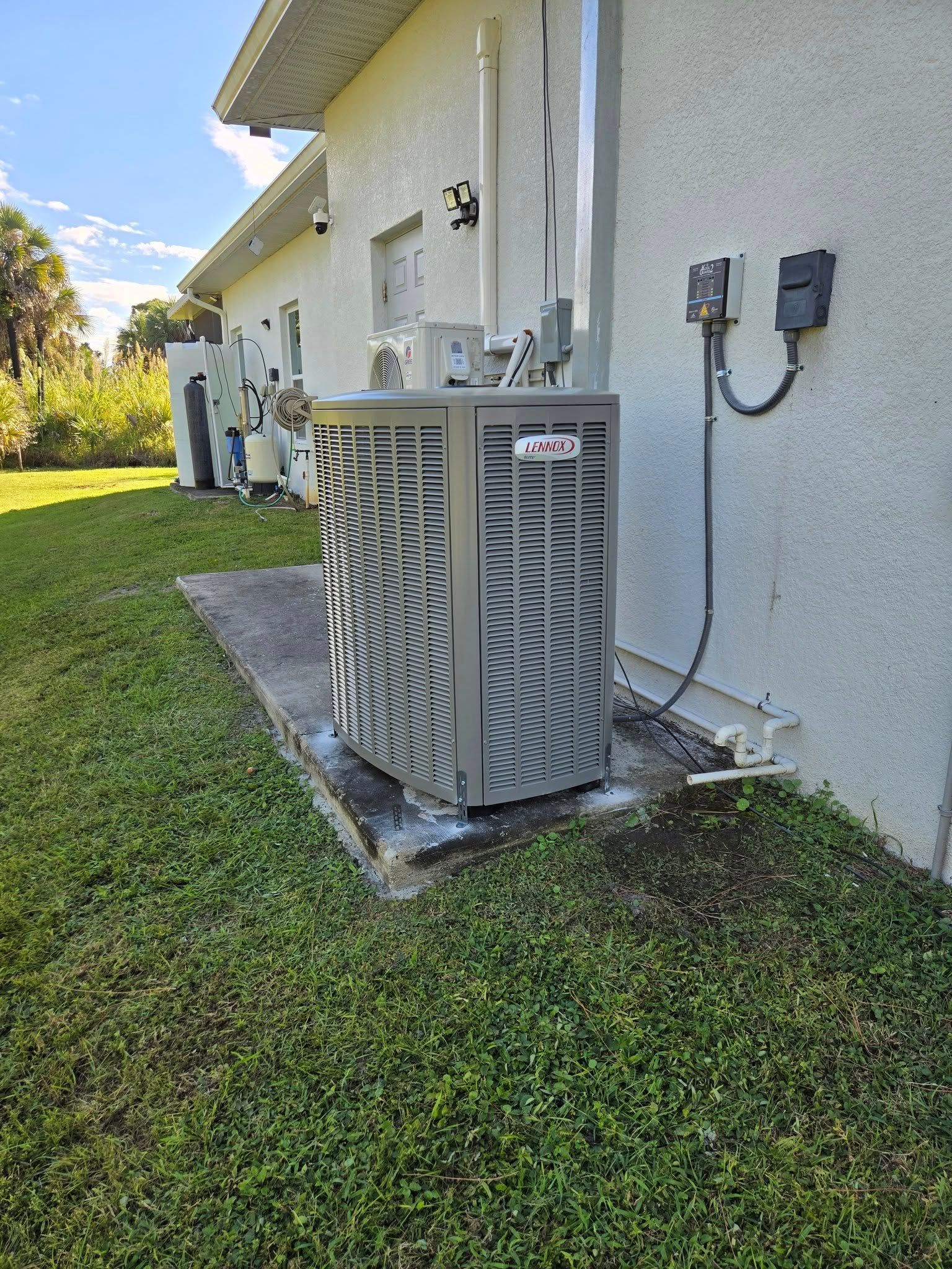 AC unit next to a light-colored building on a concrete slab, surrounded by grass and other units.