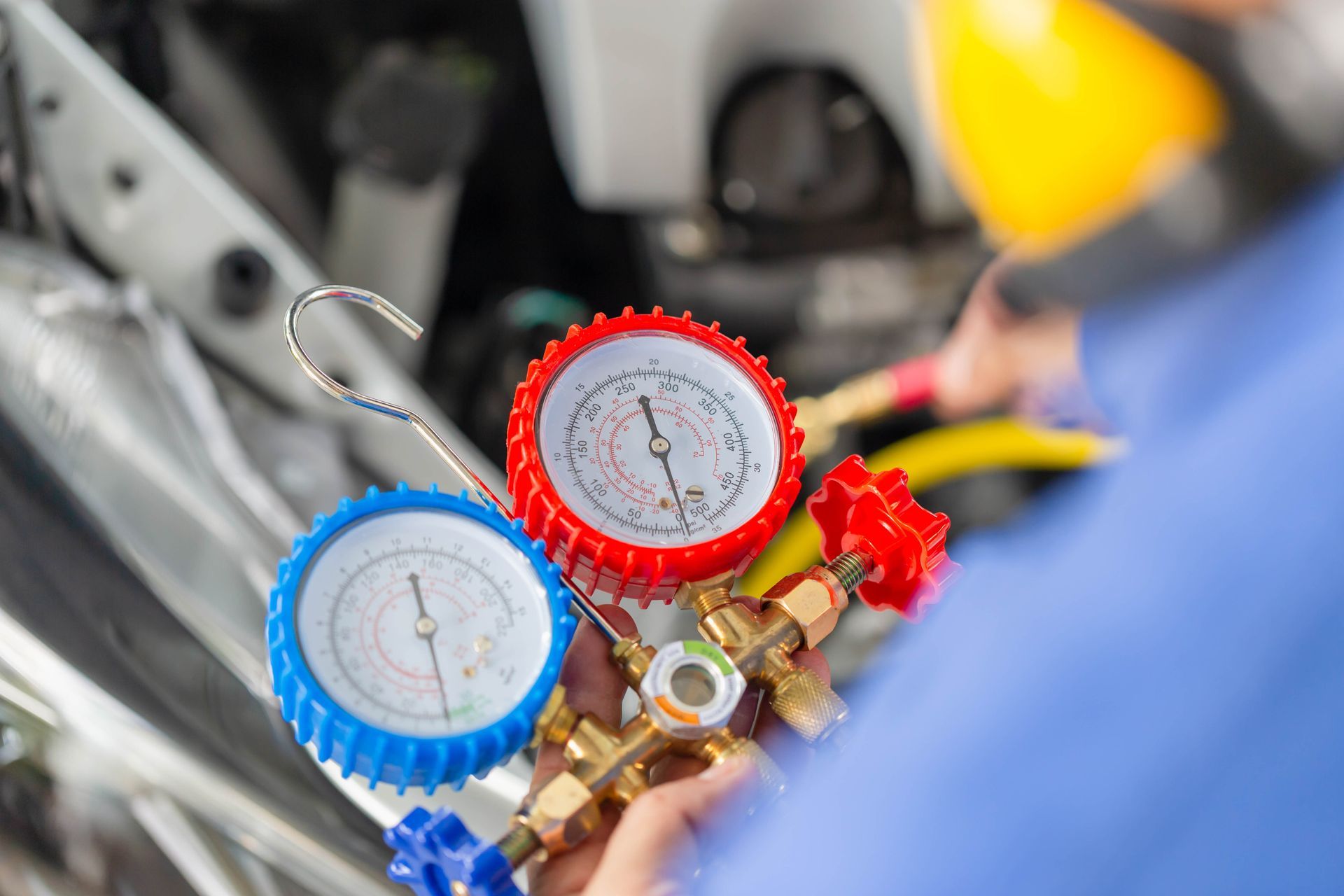 Mechanic using gauges to check car air conditioning system. Close-up on the gauges, red and blue, near engine.