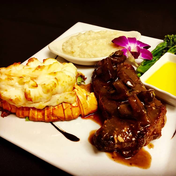 A white plate topped with a steak and a lobster tail