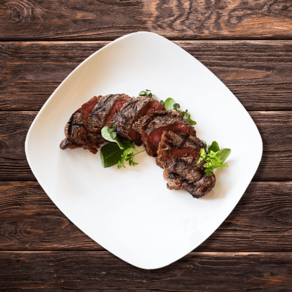 A white plate topped with sliced steak and greens on a wooden table.