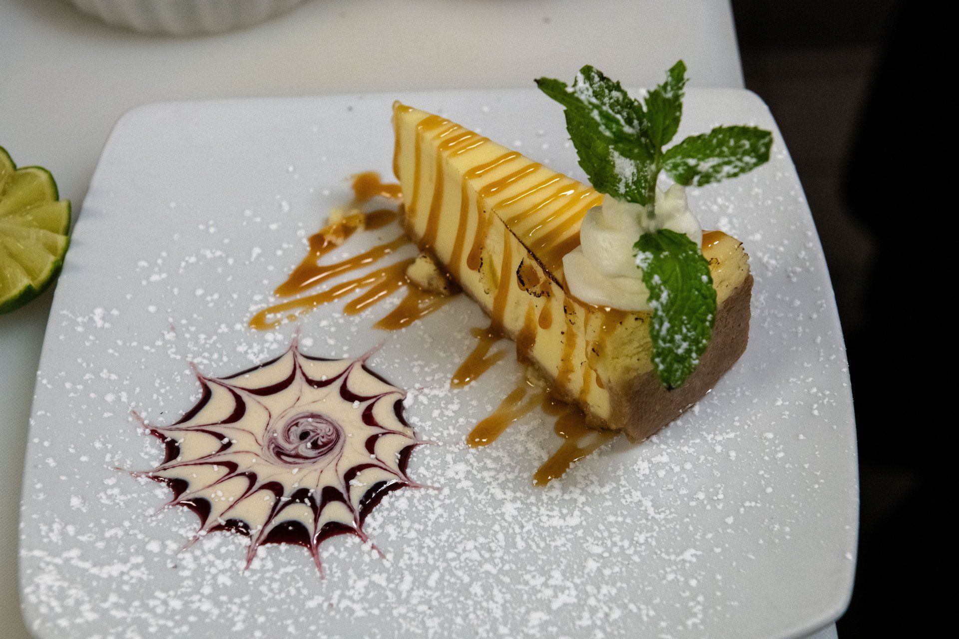 A slice of cheesecake on a white plate with powdered sugar and mint leaves