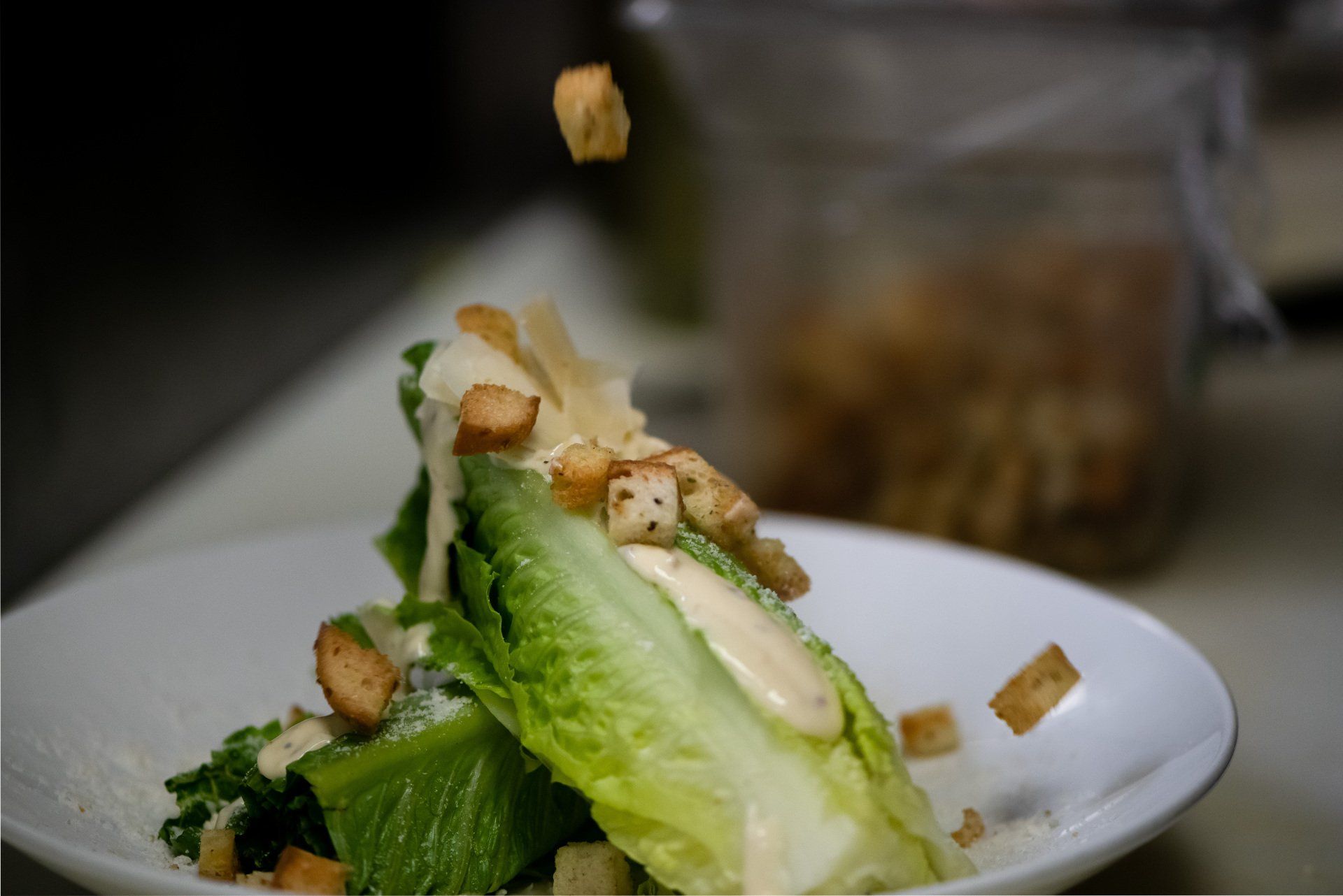 A close up of a caesar salad on a plate with croutons falling into it.