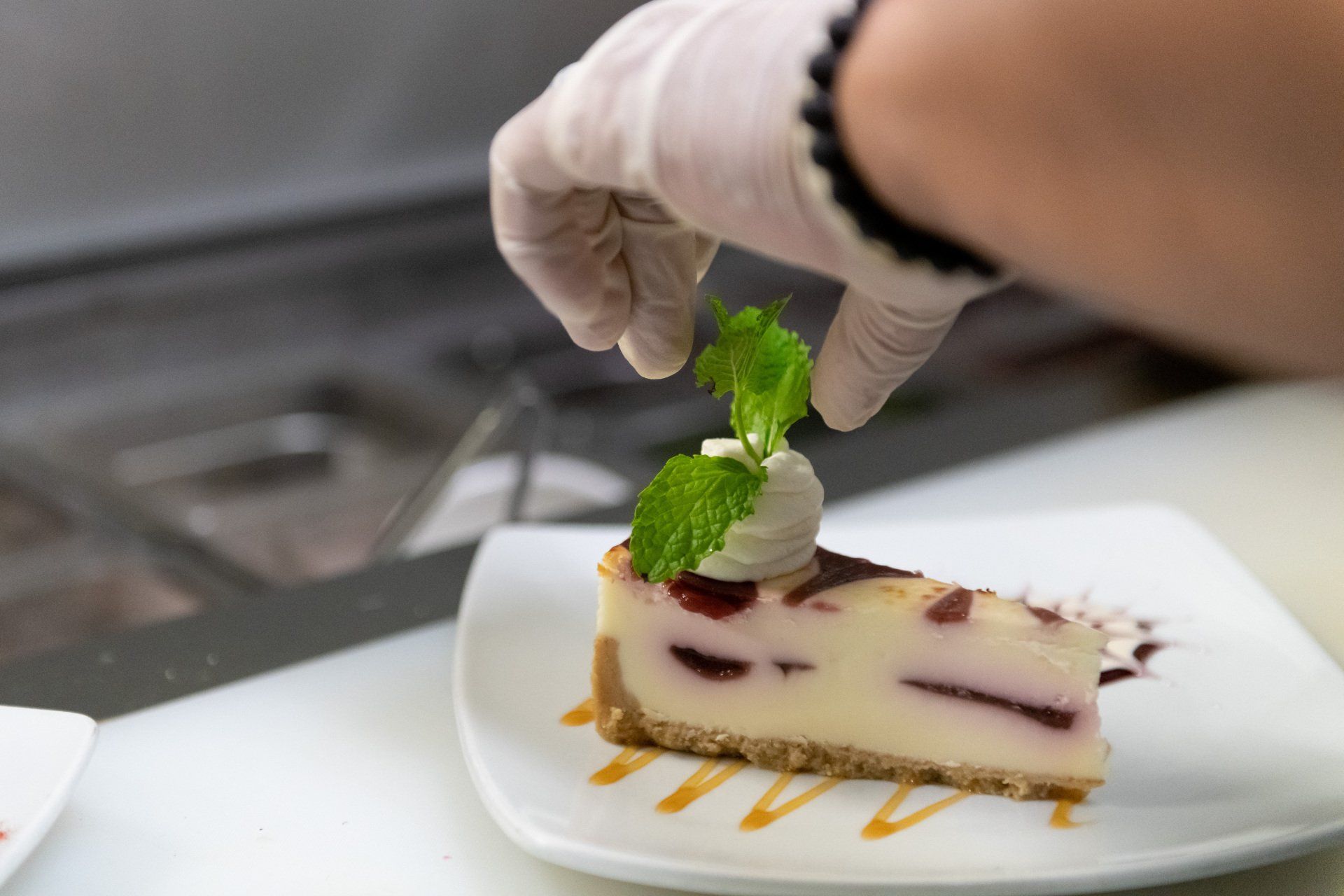 A person is decorating a cheesecake with whipped cream and mint leaves