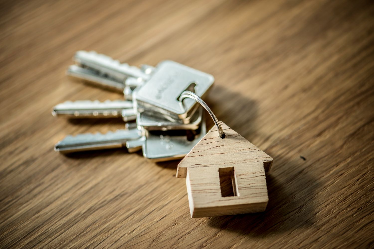 A bunch of keys with a wooden house keychain on a wooden table.