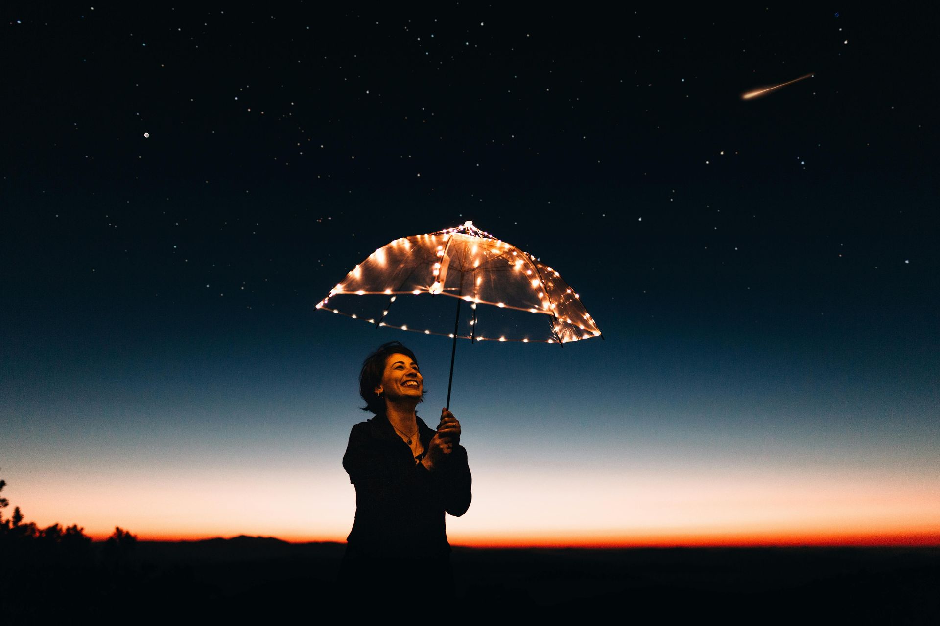 Woman looking upward, holding lit-up umbrella under starry night sky.