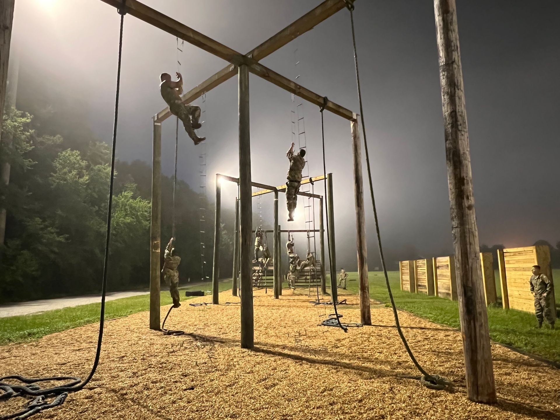 A group of people are climbing ropes on a playground at night.