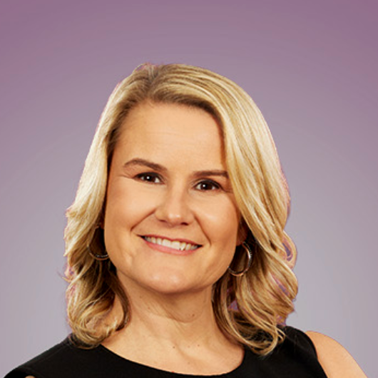 A woman wearing a black jacket and white shirt smiles for the camera