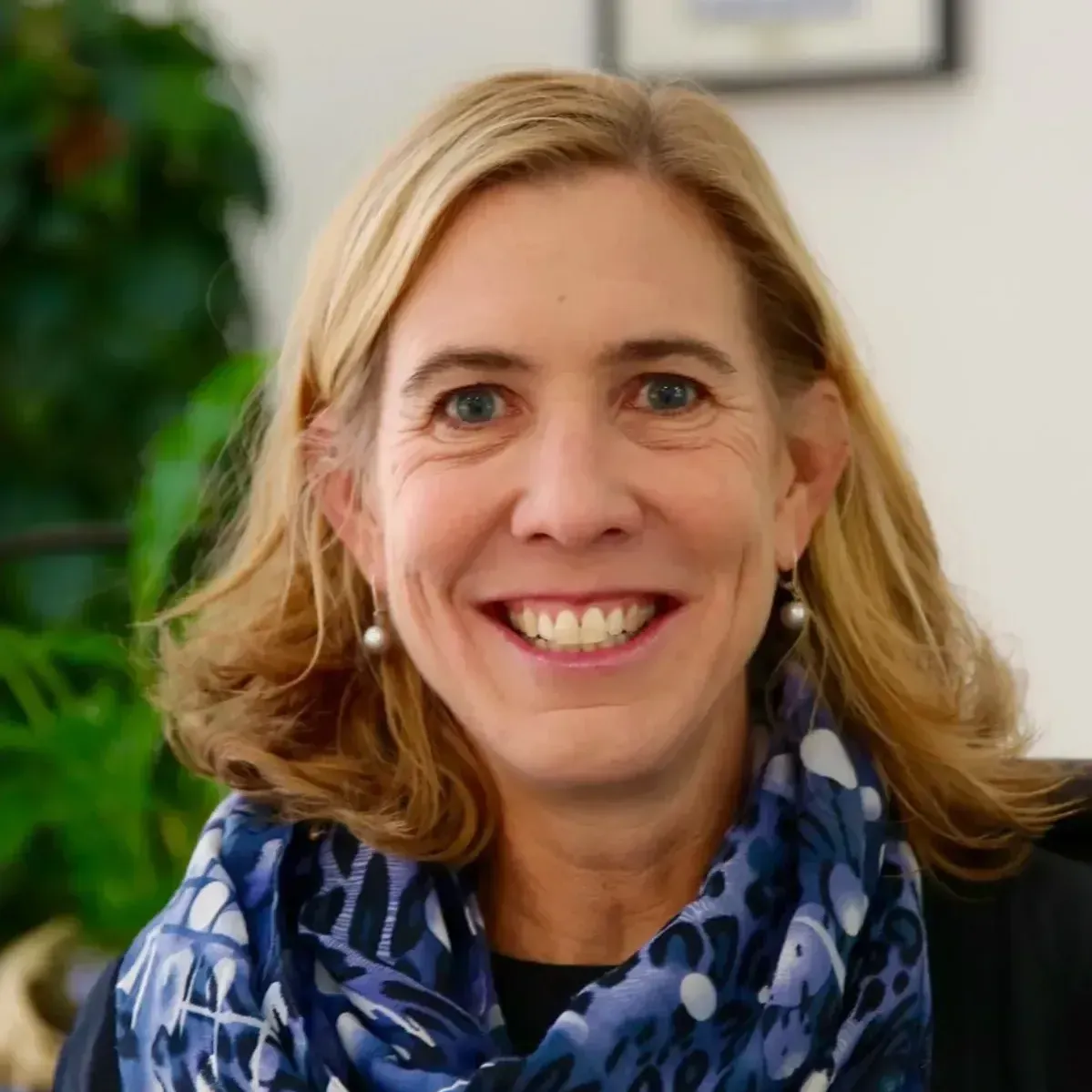 A woman wearing a blue scarf and earrings smiles for the camera