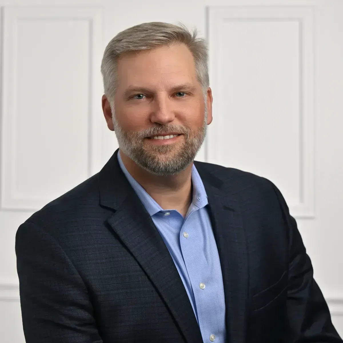 A man in a suit and blue shirt is smiling for the camera