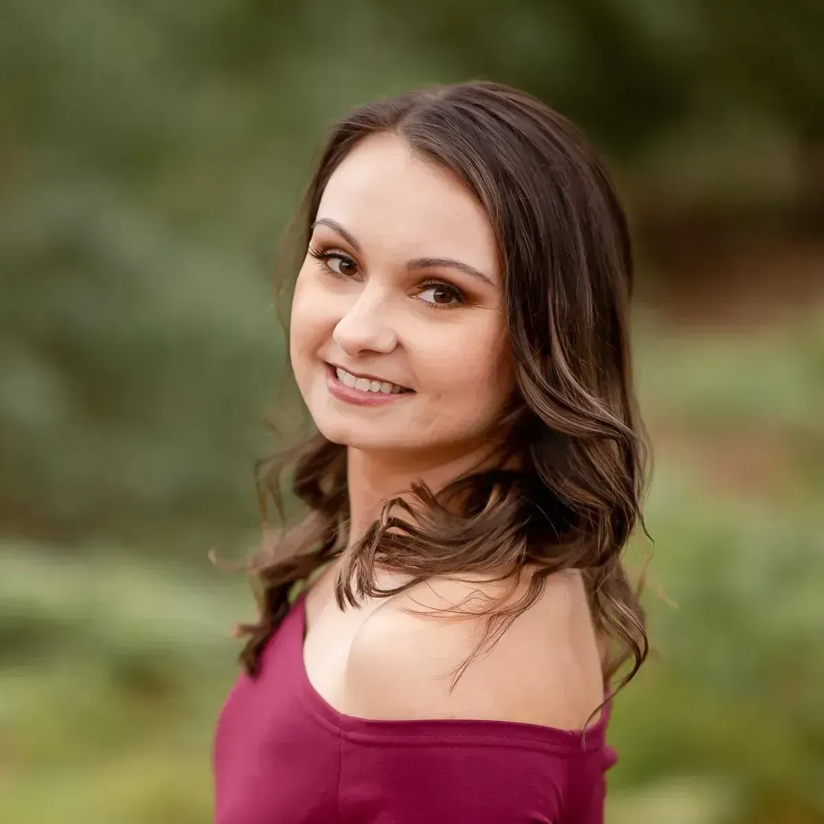 A woman in a red off the shoulder top is smiling for the camera.