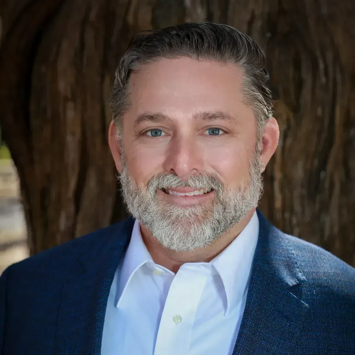 A man with a beard is wearing a suit and smiling.