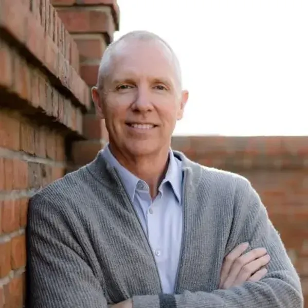 A man is leaning against a brick wall with his arms crossed.