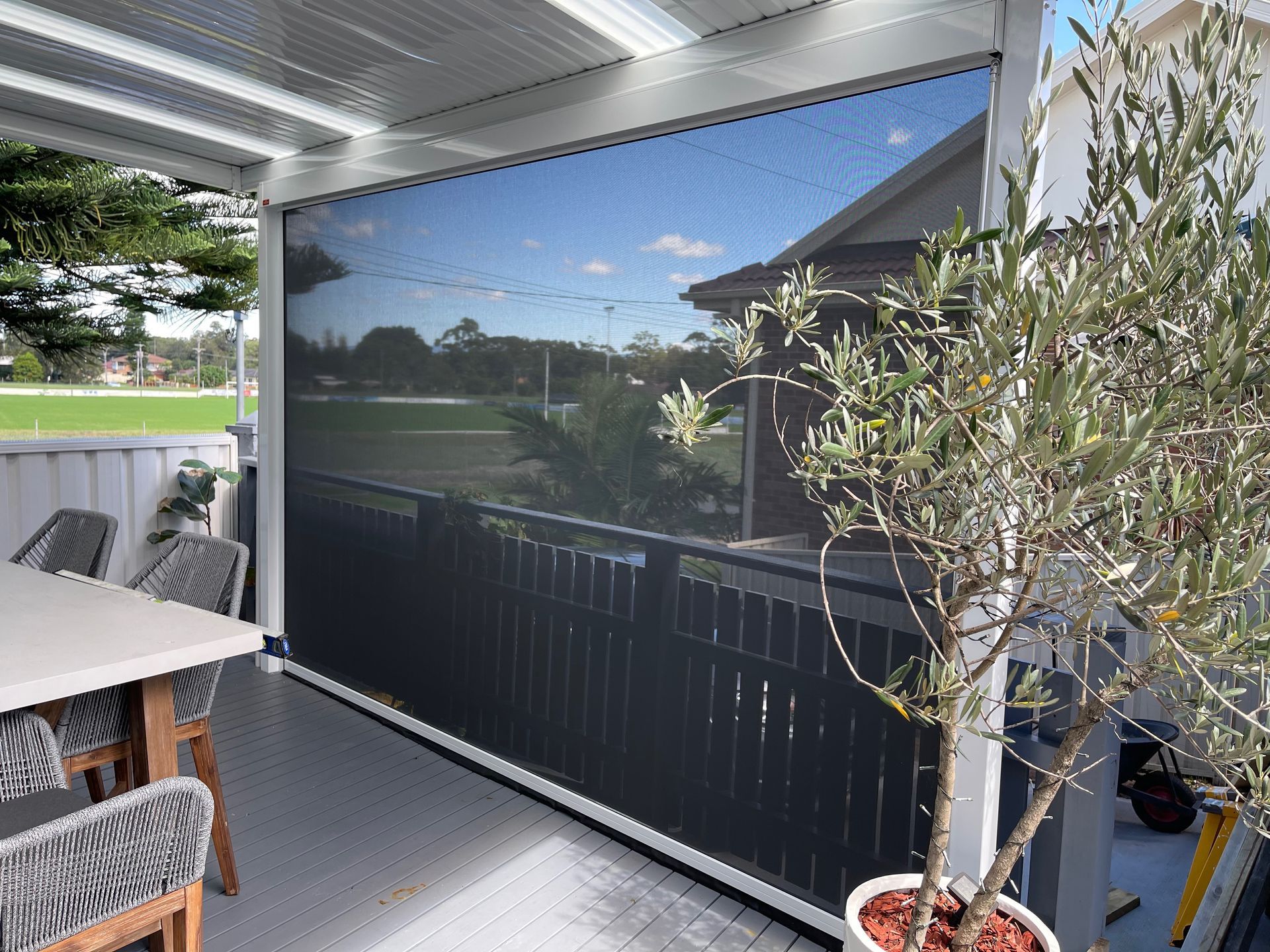 Outdoor patio with a black roller screen, table, chairs, and a potted olive tree — Narellan Home Improvement Centre In Narellan, NSW
