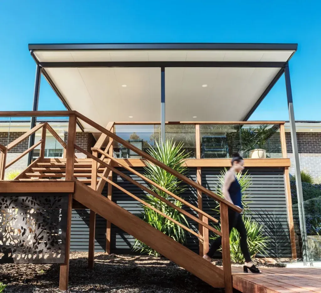 Woman Descends Wooden Stairs to a Deck With a Modern Roof — Narellan Home Improvement Centre In Narellan, NSW