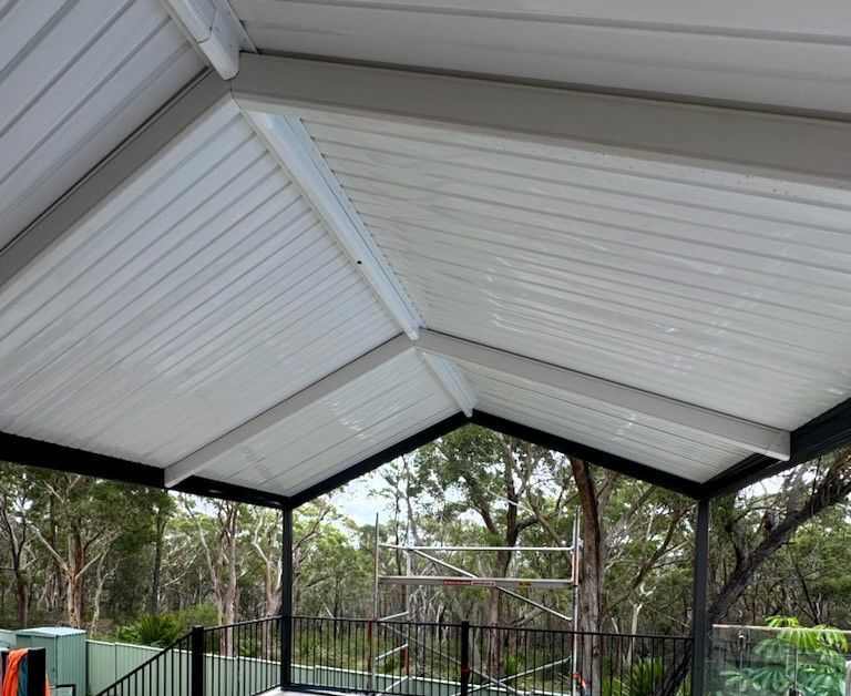 A Beige, Slatted Aluminum Pergola Cover Attached to a Blue House — Narellan Home Improvement Centre In Narellan, NSW