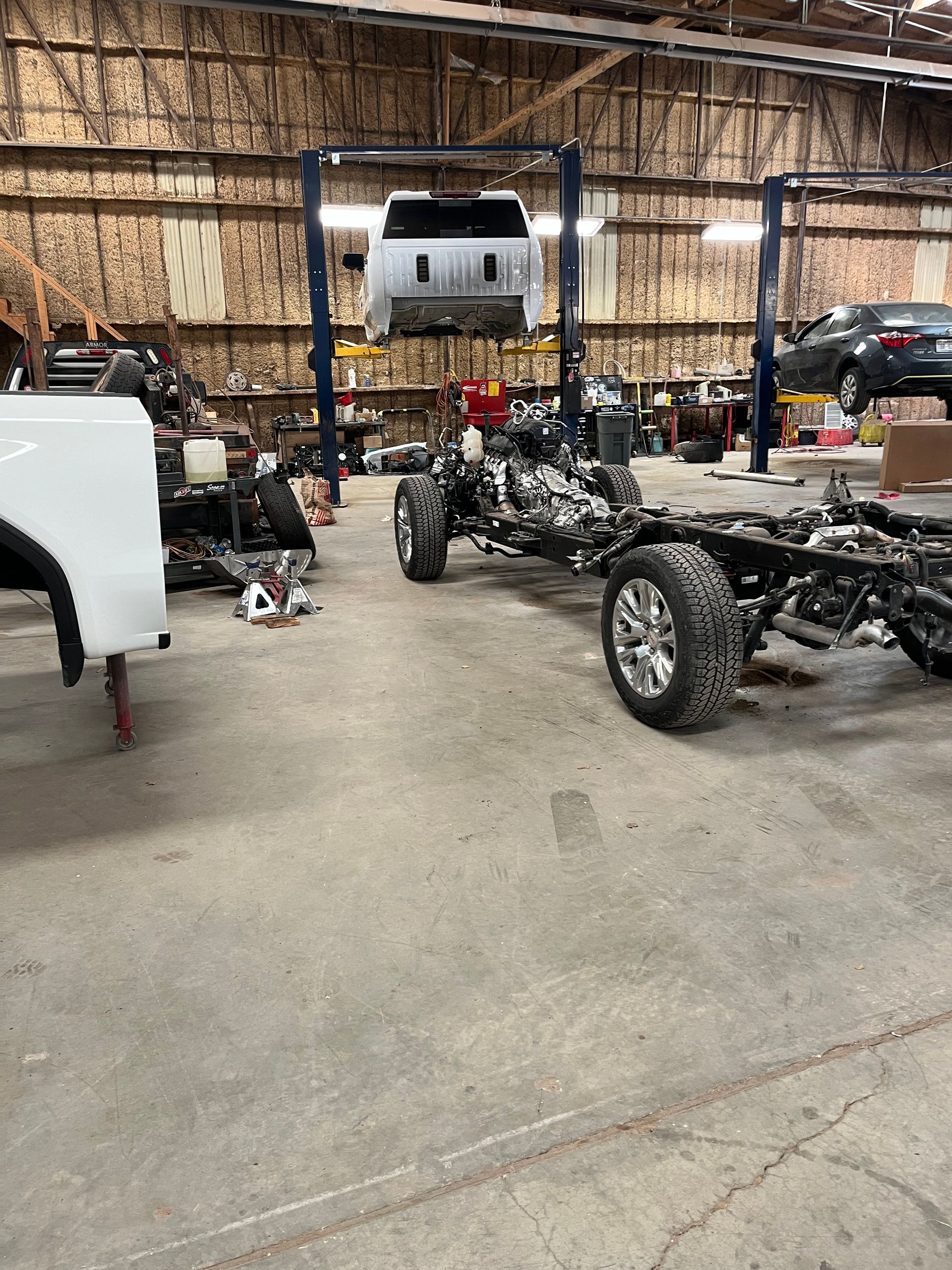 Auto shop with several vehicles and car frames inside a large warehouse | Texas Carworx
