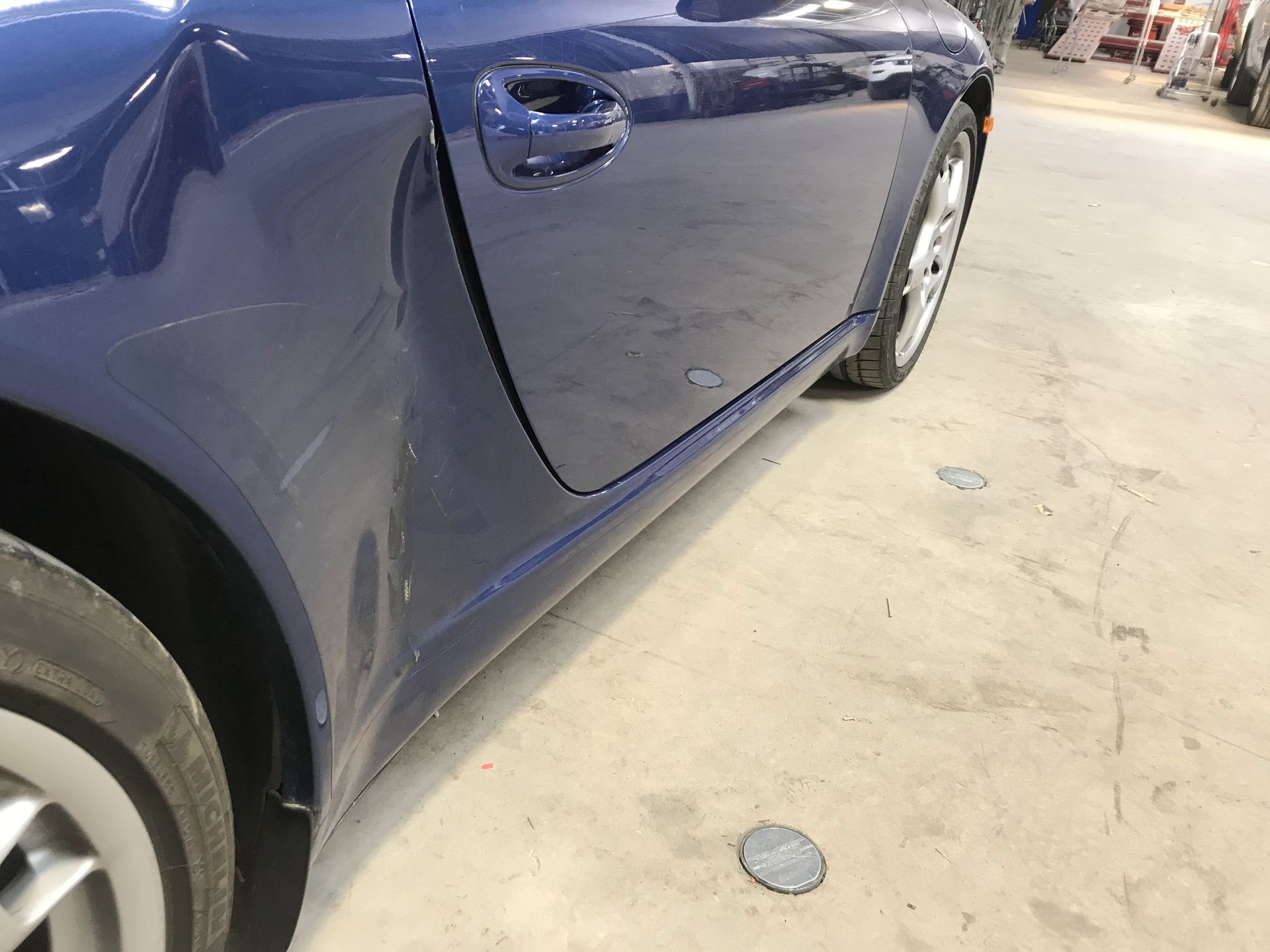 Close-up of a dark blue car door and side panel in a garage or workshop, with the front wheel visible | Texas Carworx
