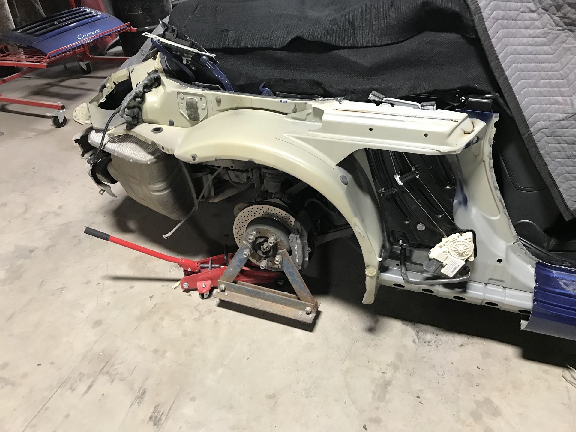 Damaged car front end in a workshop, with wheel removed and a jack stand supporting the frame | Texas Carworx