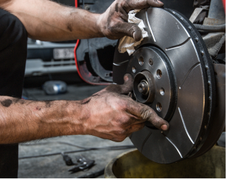 Mechanic installing a brake rotor on a car wheel hub with gloved hands in a garage | Texas Carworx