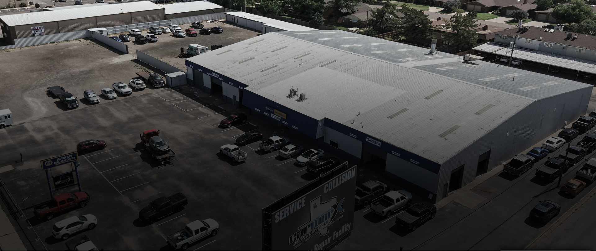 Blue SUV on a car lift inside an auto repair shop, with a dark car in the foreground.